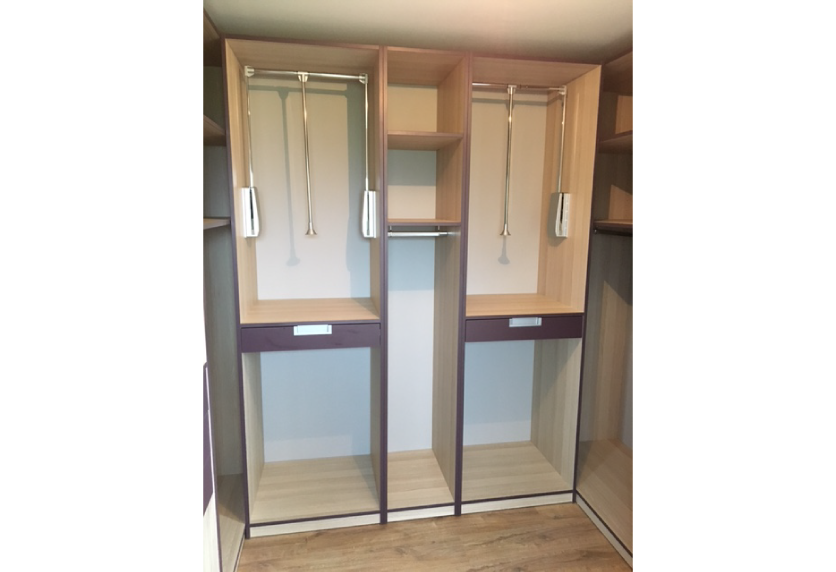 Agencement intérieur d’un dressing en bois clair avec penderies éclairées, étagères centrales et façades miroir, vers Clèdes