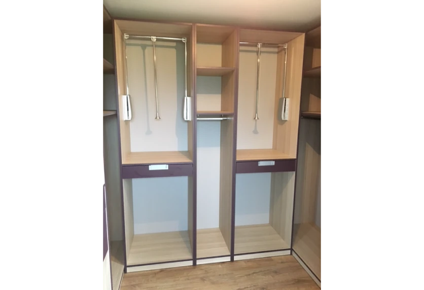 Agencement intérieur d’un dressing en bois clair avec penderies éclairées, étagères centrales et façades miroir, vers Clèdes
