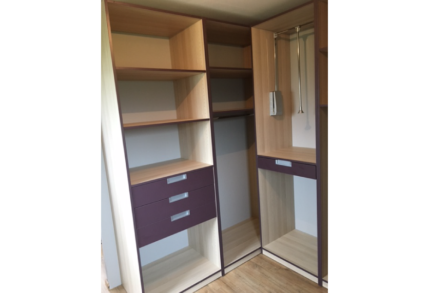 Dans un dressing à Pimbo, agencement intérieur associant penderie, étagères en bois clair et tiroirs contrastés