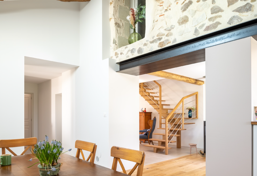 À Samadet, agencement intérieur d’une pièce ouverte où un escalier en bois apparaît sous une poutre sombre