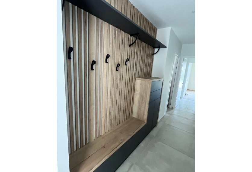 Agencement intérieur pour une entrée à Garlin : mur à tasseaux de bois, patères noires et banc intégré