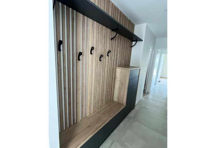 Agencement intérieur pour une entrée à Garlin : mur à tasseaux de bois, patères noires et banc intégré