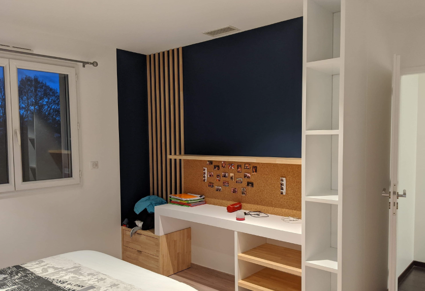 Agencement intérieur d’une chambre à Pimbo avec bureau en bois, mur bleu foncé et étagère blanche