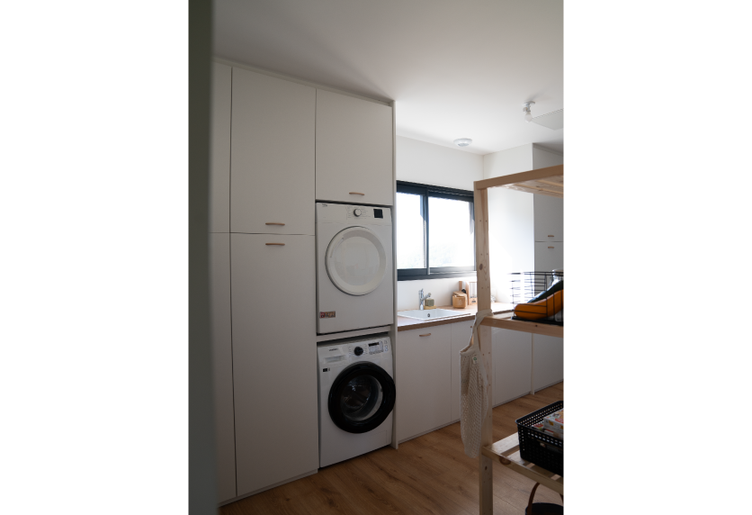 Pour une buanderie à Samadet, placards blancs intégrant un lave-linge et un sèche-linge dans l’agencement intérieur