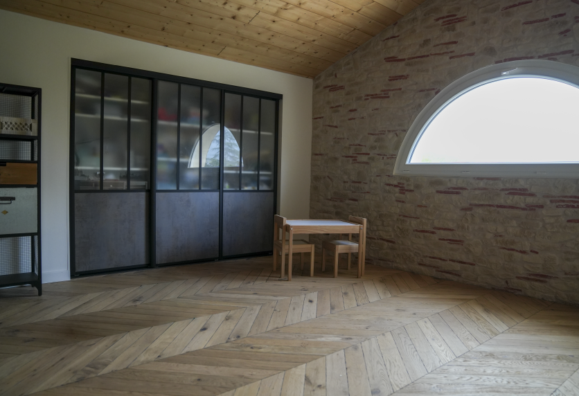 Dans une pièce aux murs en pierre à Lauret, verrière noire vitrée intégrée à l’agencement intérieur