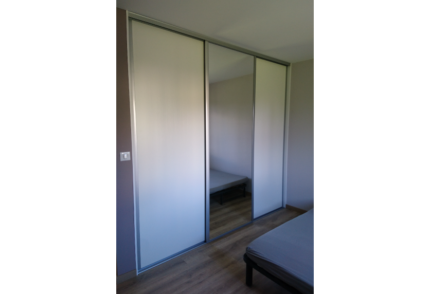 Agencement intérieur d’une chambre à Garlin avec placard coulissant clair et porte centrale en miroir