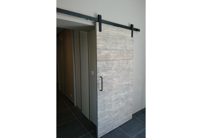 Pour une maison à Hagetmau, agencement intérieur avec porte coulissante aspect bois gris sur rail noir apparent