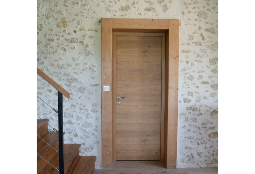 À Serres-Gaston, porte intérieure en bois clair encadrée par un mur en pierre dans un projet d’agencement intérieur