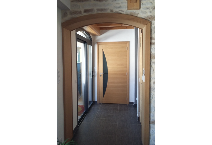 Sous une arche en pierre à Samadet, agencement intérieur d’un couloir avec porte en bois et vitrage courbe