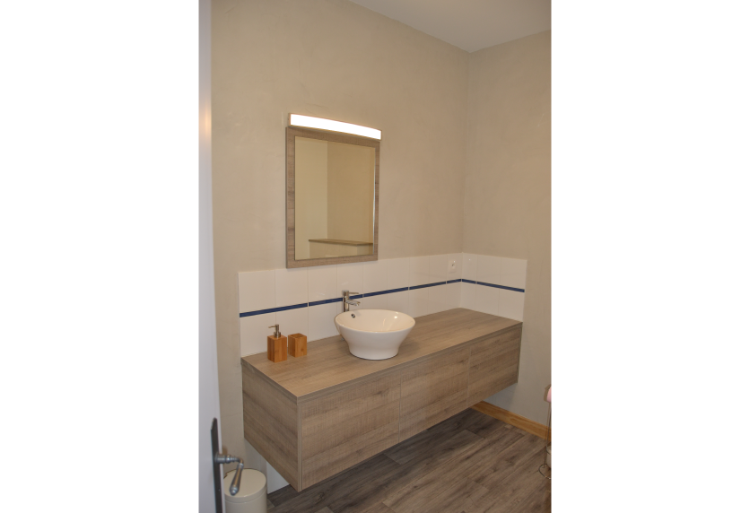 À Serres-Gaston, agencement intérieur d’une salle d’eau avec meuble suspendu aspect bois et vasque blanche