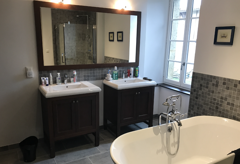 À Geaune, deux meubles vasques foncés et un grand miroir composent l’agencement intérieur de cette salle de bain