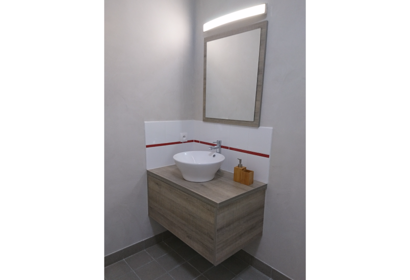 Meuble vasque suspendu gris sous un miroir éclairé, détail d’agencement intérieur pour une salle d’eau à Clèdes