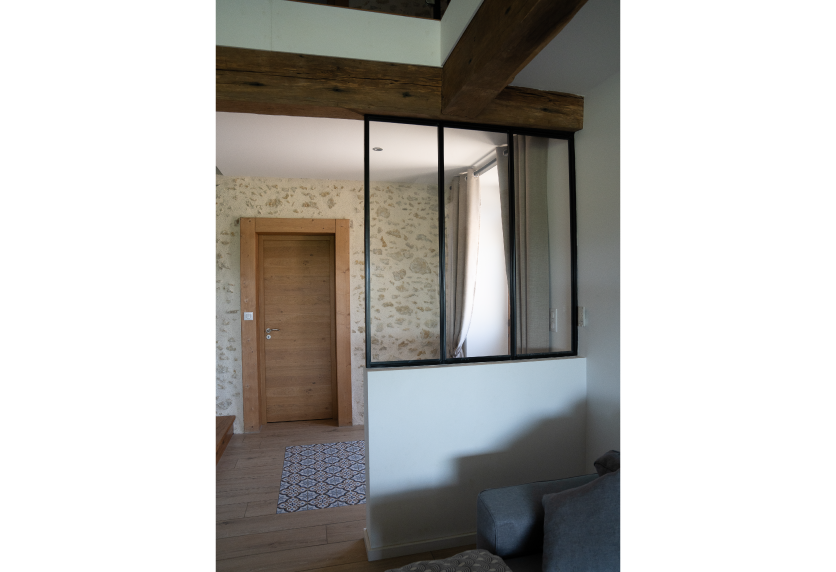 Agencement intérieur avec verrière noire sur muret blanc, entre le salon et un passage aux murs de pierre, pour un projet à Hagetmau.