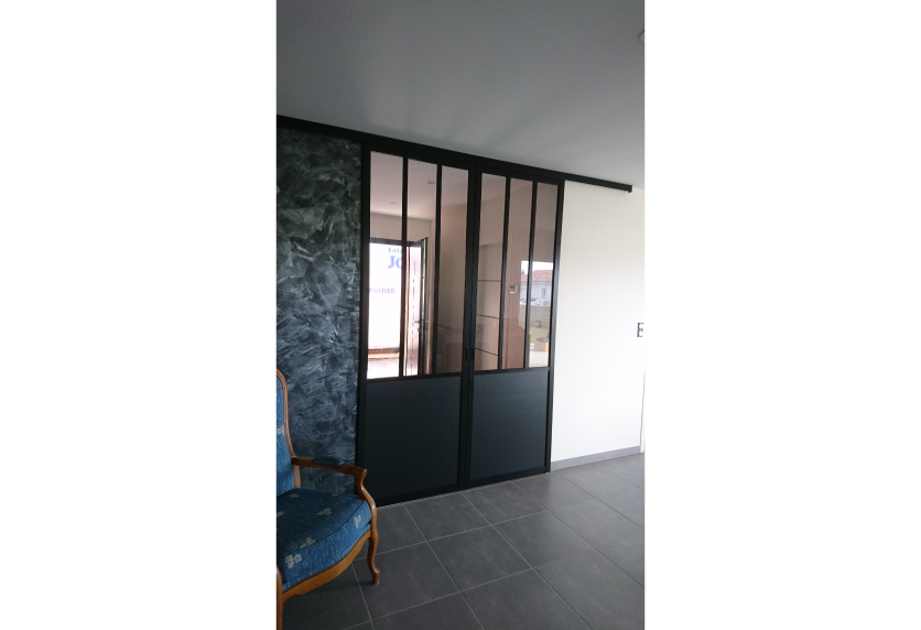 À Castelnau-Tursan, cette cloison vitrée noire avec porte intégrée sépare deux pièces dans un agencement intérieur.