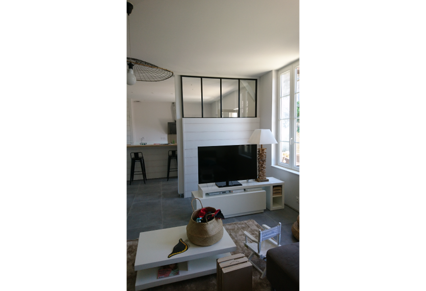 Agencement intérieur à Geaune : une verrière noire surmonte la cloison du salon et laisse voir la cuisine.