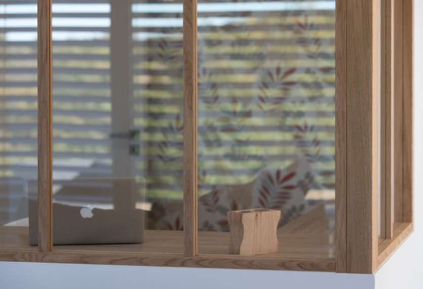 Agencement intérieur pour un séjour à Garlin, avec verrière à cadre bois, tablette pour les plantes et vue sur la pièce voisine.