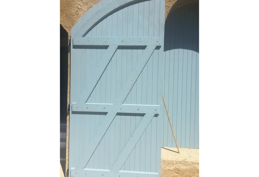 Volet bleu clair à sommet cintré et ferrures apparentes : une menuiserie en bois pour une façade à Miossens-Lanusse