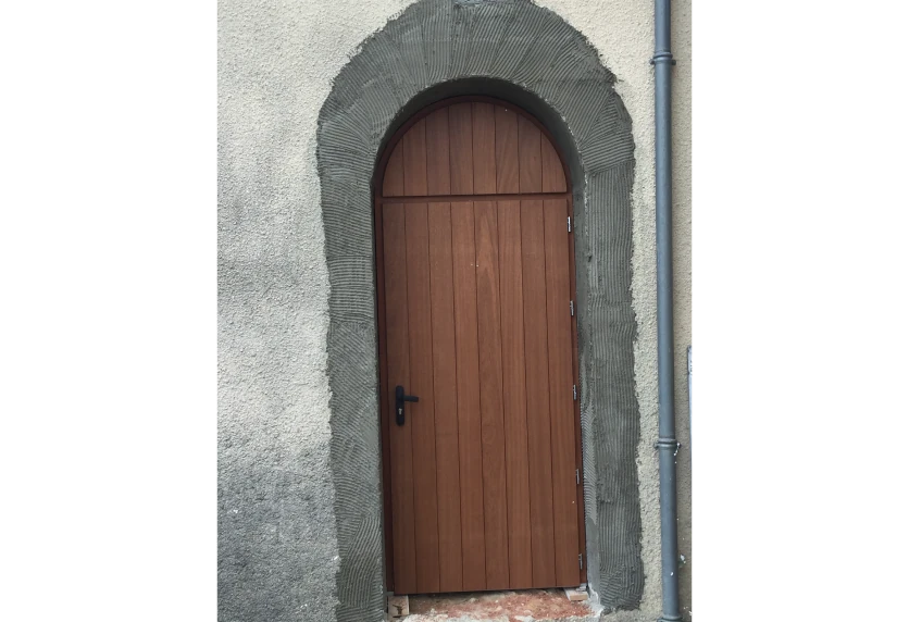 Pour une maison à Thèze, porte de menuiserie en bois à sommet arrondi dans un encadrement en pierre