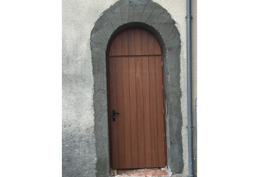 Pour une maison à Thèze, porte de menuiserie en bois à sommet arrondi dans un encadrement en pierre