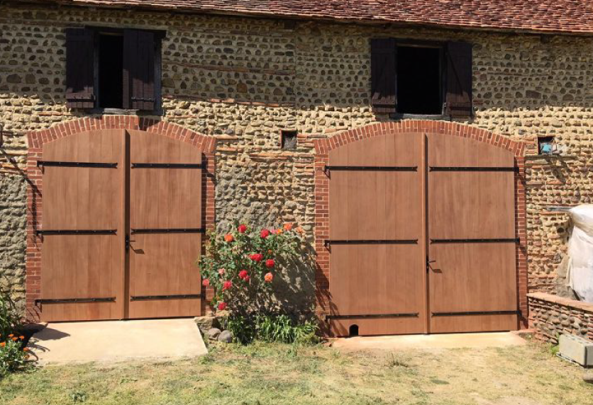 Sur une dépendance à Garlin, deux portes de menuiserie en bois avec ferrures noires habillent une façade en pierre