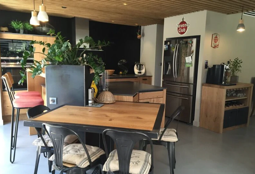 Cuisine ouverte près de Castelnau-Tursan, associant une table en bois, des chaises noires et des rangements sombres
