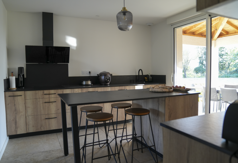 À Pimbo, cuisine avec îlot repas, meubles en bois clair et plan de travail noir