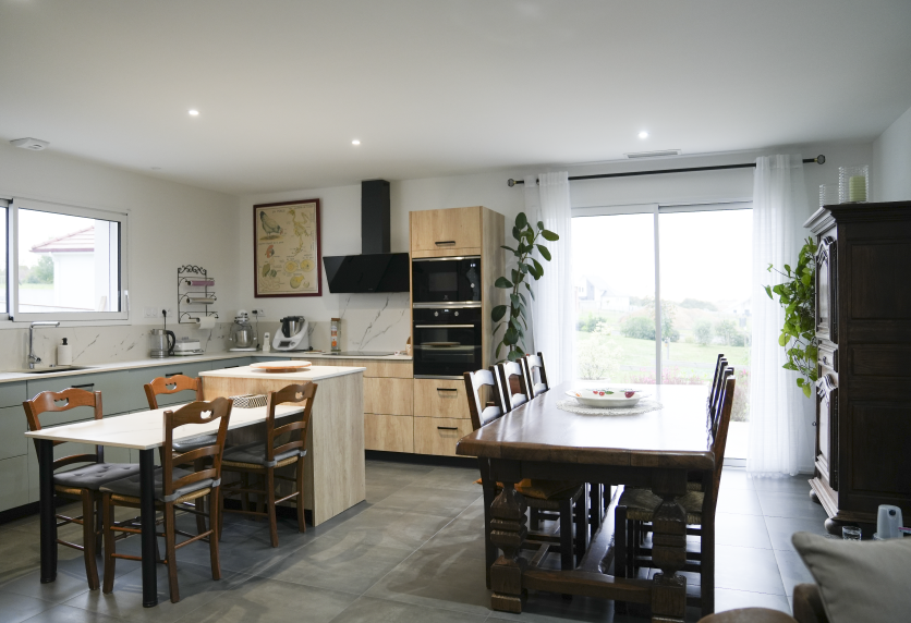 Cuisine ouverte sur la salle à manger, avec îlot en bois clair et meubles blancs, pour une maison à Lauret
