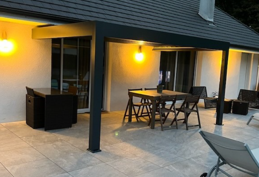 Sous une pergola anthracite, un coin repas éclairé en soirée illustre un projet de menuiserie à Hagetmau.