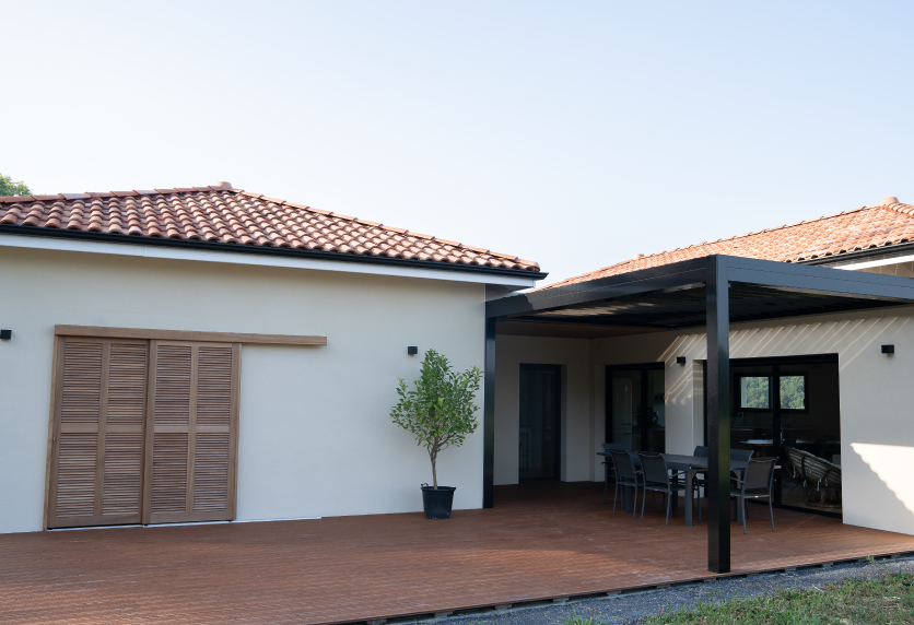 Pergola sombre adossée à la maison, au bout d’une grande terrasse en bois, pour un projet de menuiserie à Serres-Gaston.
