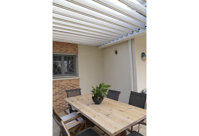 Vue sous les lames blanches d’une pergola couvrant un espace repas, dans un projet de menuiserie à Castelnau-Tursan.