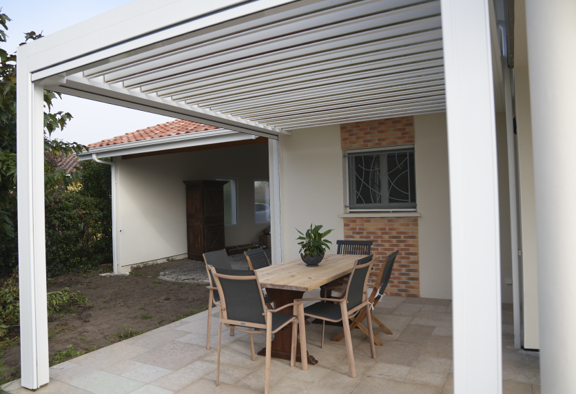 À Geaune, une pergola blanche à lames surplombe la table et les chaises disposées devant la maison.