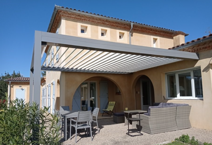 ergola blanche à lames installée devant une maison aux ouvertures cintrées, pour une menuiserie à Clèdes.