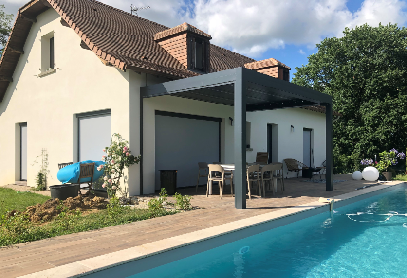 À Lauret, pergola anthracite aménagée près de la piscine et attenante à une maison claire.