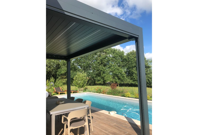 À Garlin, pergola sombre au bord de la piscine, avec table haute sous la toiture et terrasse en bois.