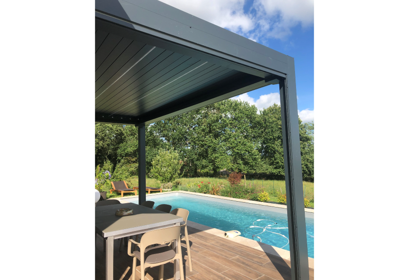 À Garlin, pergola sombre au bord de la piscine, avec table haute sous la toiture et terrasse en bois.