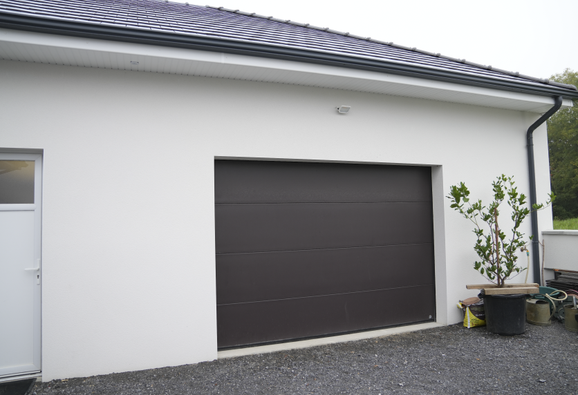 Porte de garage gris anthracite intégrée à la façade blanche d’une maison, pour un projet de menuiserie à Hagetmau.