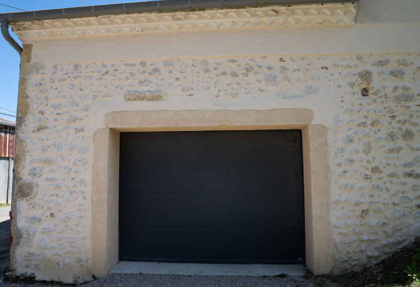 À Audignon, une porte de garage sombre s’inscrit dans l’ouverture en pierre d’un bâtiment ancien.