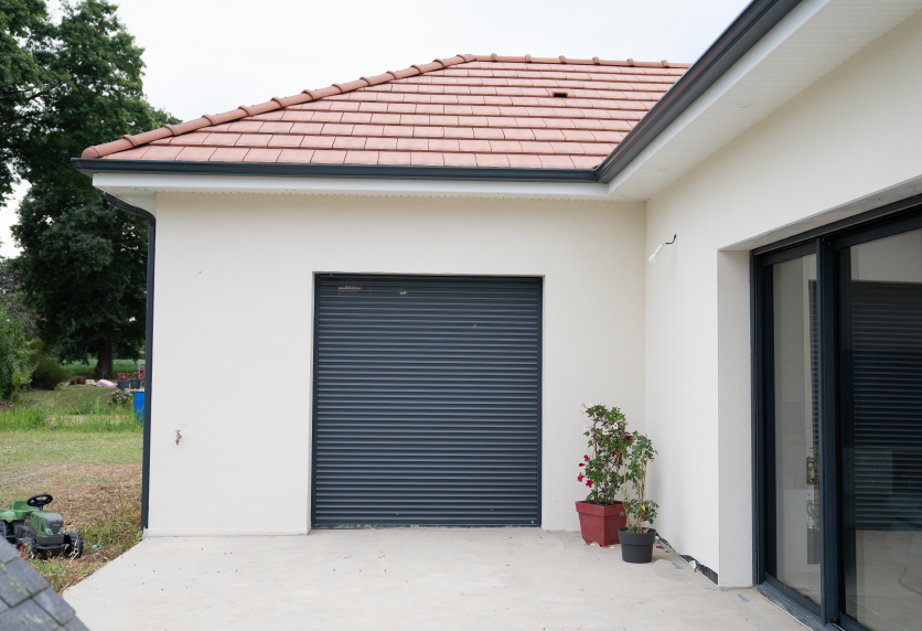 Porte de garage grise près d’une baie vitrée, sur la façade claire d’une maison à Serres-Gaston.