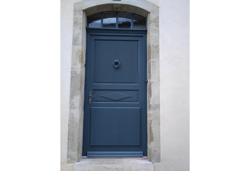 Dans un encadrement en pierre, porte d’entrée bleu foncé avec imposte vitrée, exemple de menuiserie pour une maison à Pau