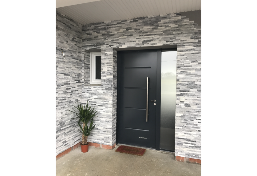 Pour une entrée à Doumy, porte de menuiserie anthracite à poignée verticale devant une façade en parement de pierre