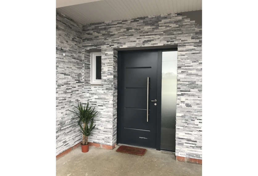 Pour une entrée à Doumy, porte de menuiserie anthracite à poignée verticale devant une façade en parement de pierre