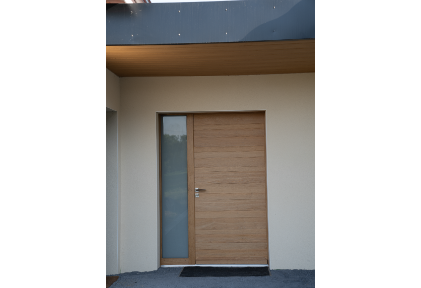 Porte d’entrée aspect bois avec vitrage latéral étroit, un choix de menuiserie pour une façade à Thèze