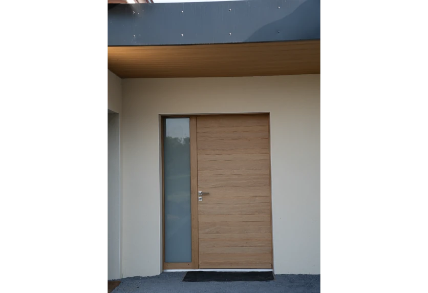 Porte d’entrée aspect bois avec vitrage latéral étroit, un choix de menuiserie pour une façade à Thèze