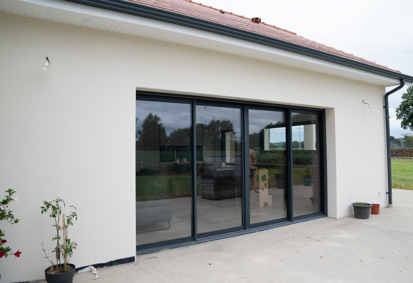 Grande baie vitrée aux profilés foncés donnant sur une terrasse, exemple de menuiserie pour une maison à Lons