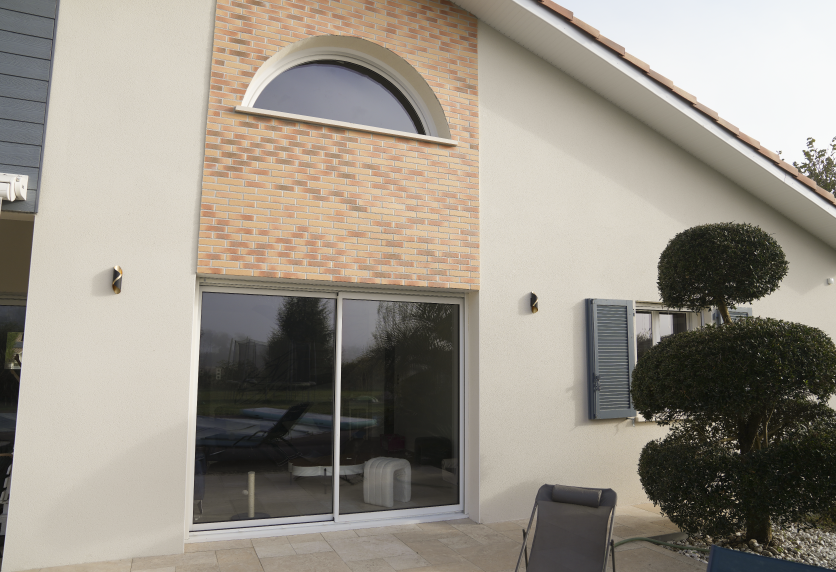 Pour une façade à Montardon, baie coulissante vitrée sous une fenêtre cintrée, dans un ensemble de menuiserie contemporain