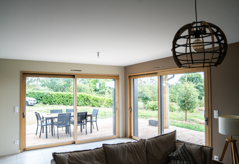 Dans un salon ouvert sur le jardin à Thèze, la menuiserie vitrée laisse entrer la lumière par deux grandes baies