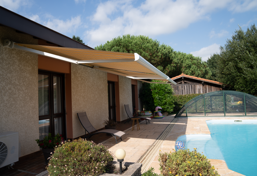 Store banne à toile ocre déployé au-dessus d’une terrasse avec piscine, parmi les solutions de menuiserie extérieure proposées près de Pau