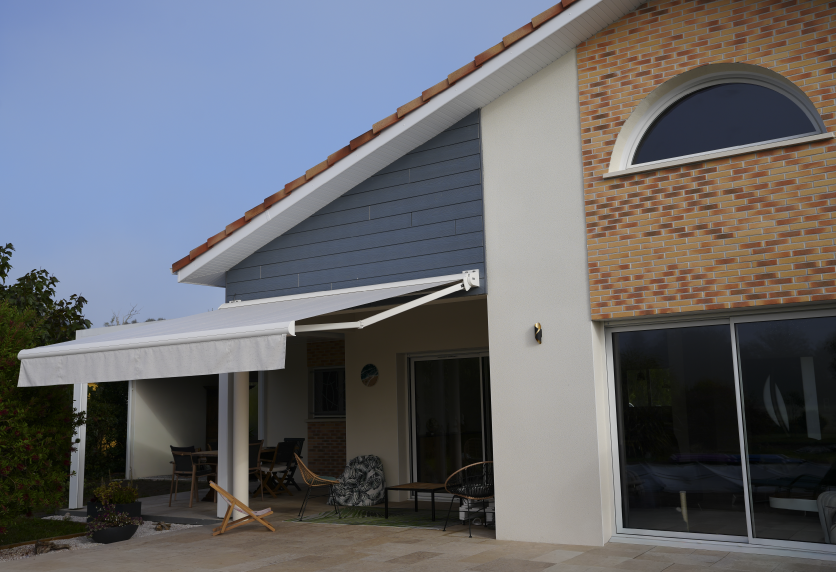 Pour une terrasse à Serres-Castet, store banne blanc fixé à la façade, associé aux menuiseries vitrées de la maison